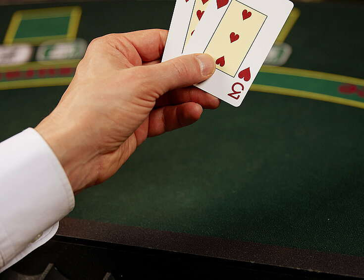 Dealer-Hände mit zwei Poker-Karten: Zehn und Drei am Poker-Tisch mit Jetons