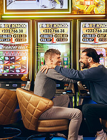 Zwei Männer sitzen vor den Fort Knox Spielautomaten von Casinos Austria
