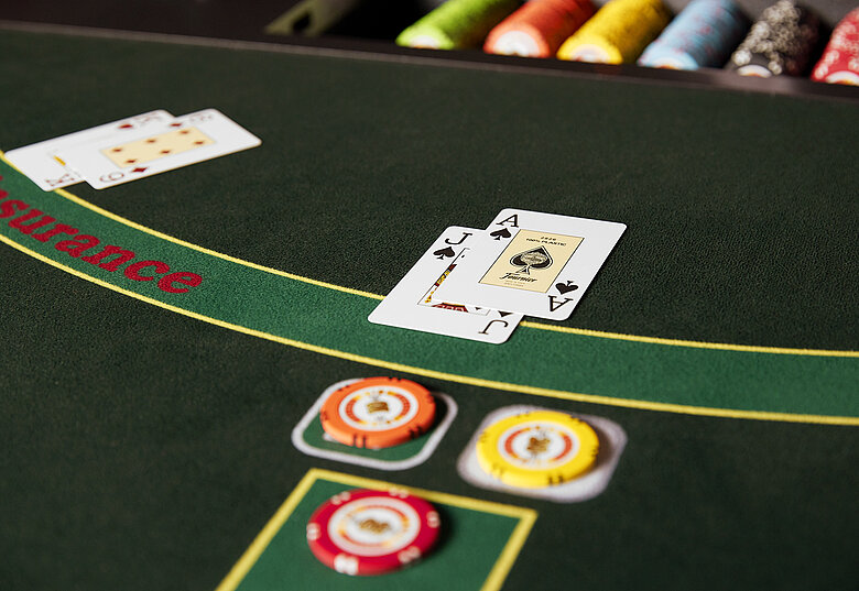 Blackjack-Tisch mit Ass und Bube auf grünem Filz, begleitet von bunten Jetons.