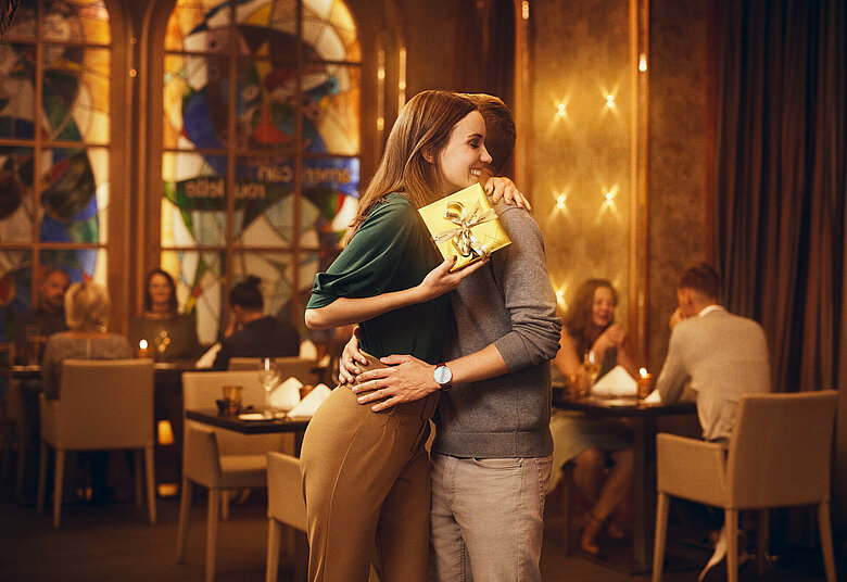 Dame mit Geschenk umarmt Mann im Casino Restaurant