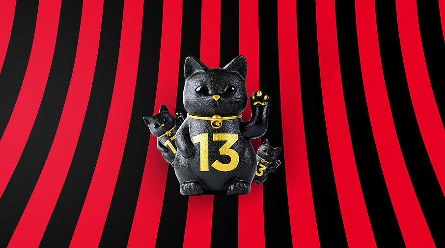 Eine große und zwei kleine schwarze Glückskatzen mit goldener 13 auf rot-schwarz-gestreiftem Hintergrund