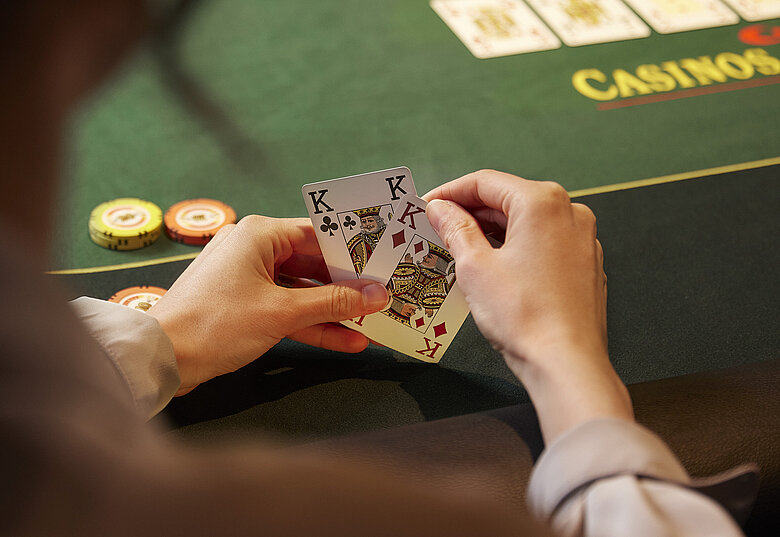 Pokerspieler:in mit 2 Karten in den Händen vor Poker-Tisch