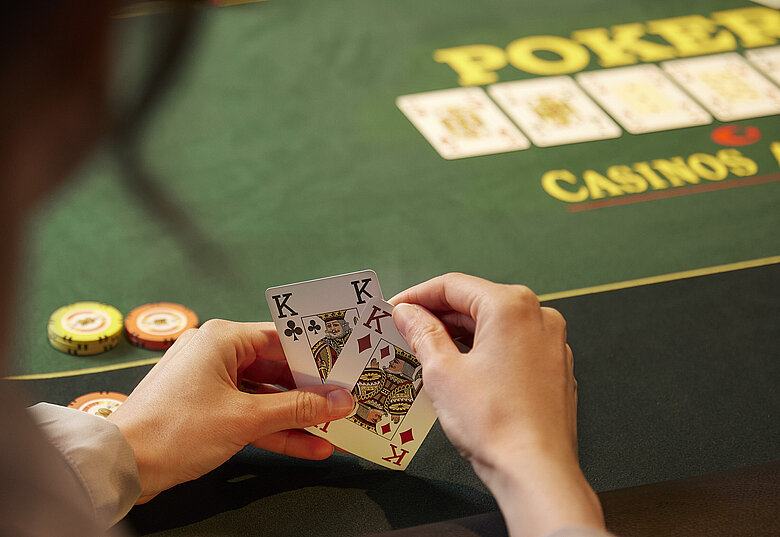Pokerspieler:in mit 2 Karten in den Händen vor Poker-Tisch