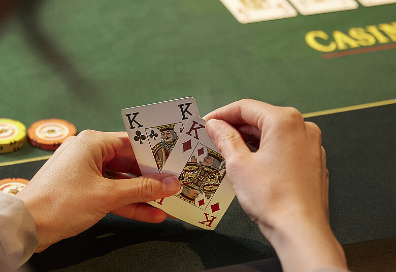 Pokerspieler:in mit 2 Karten in den Händen vor Poker-Tisch