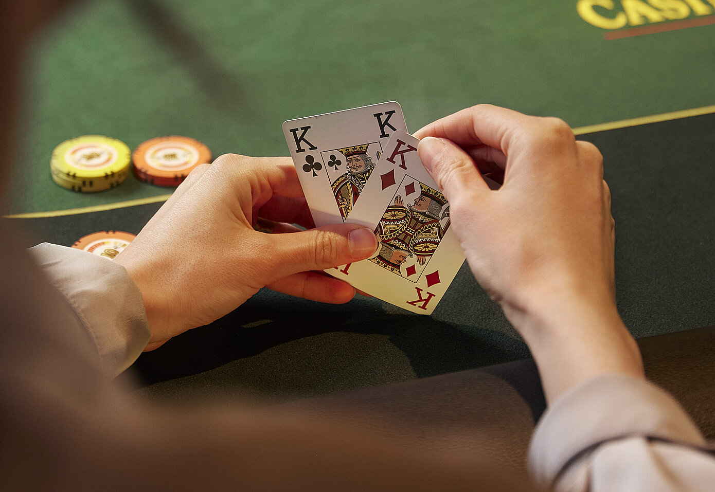 Pokerspieler:in mit 2 Karten in den Händen vor Poker-Tisch