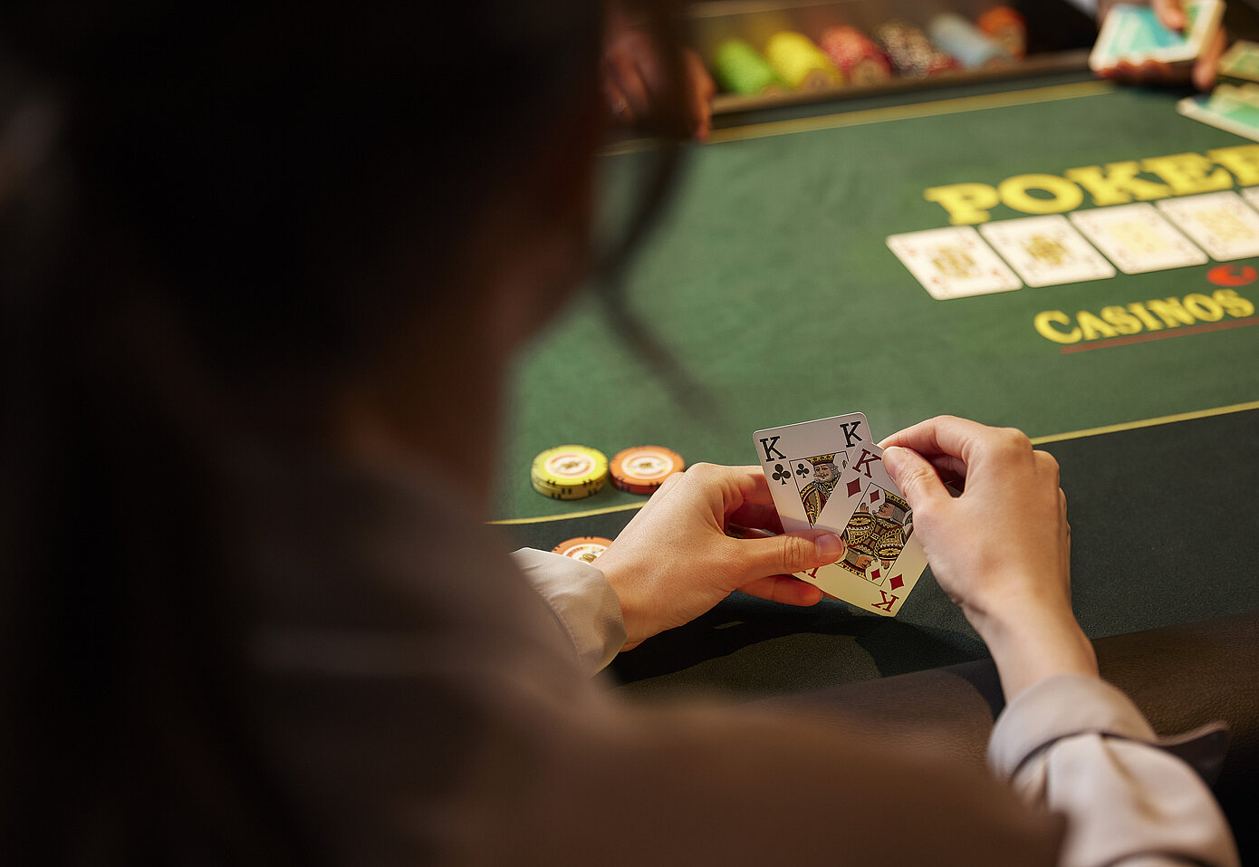 Pokerspieler:in mit 2 Karten in den Händen vor Poker-Tisch