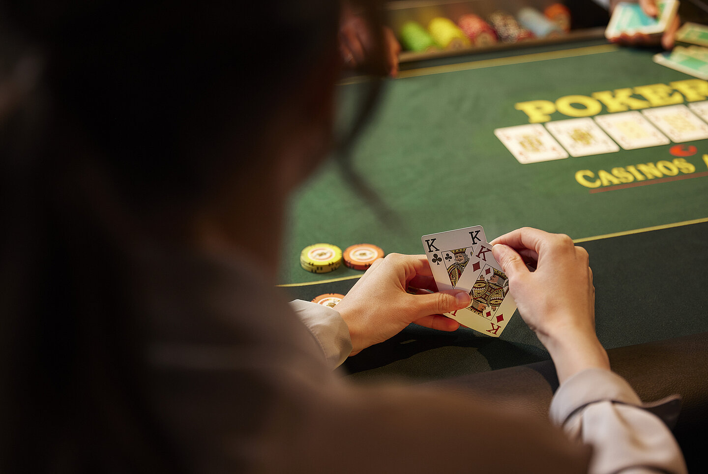 Pokerspieler:in mit 2 Karten in den Händen vor Poker-Tisch