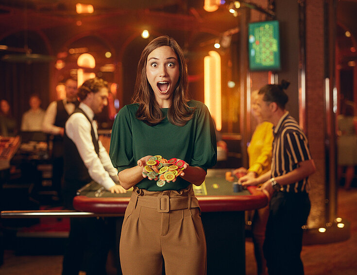 Casinos Austria Dame im Casino mit großen Augen und weit geöffnetem Mund hält Jetons in Händen