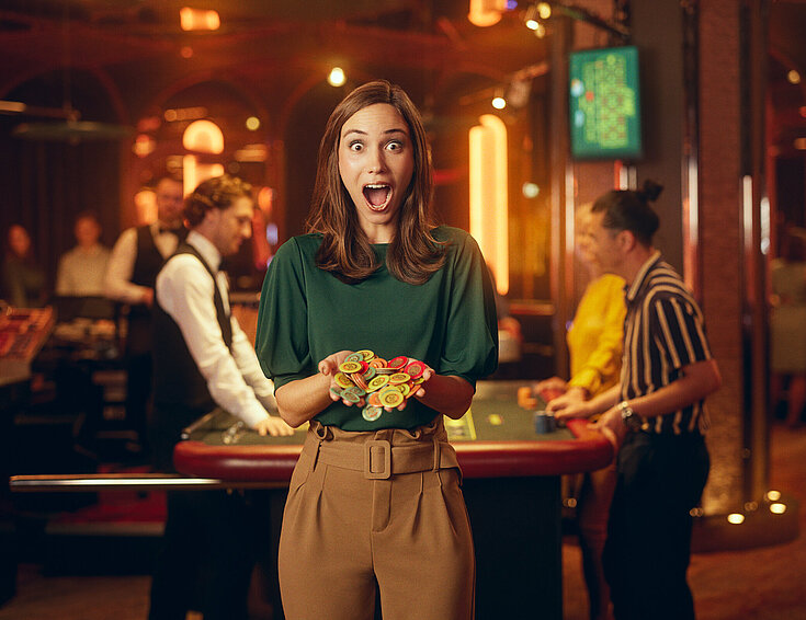 Casinos Austria Dame im Casino mit großen Augen und weit geöffnetem Mund hält Jetons in Händen