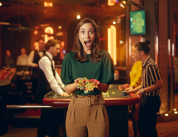 Casinos Austria Dame im Casino mit großen Augen und weit geöffnetem Mund hält Jetons in Händen