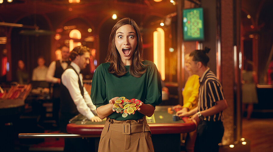 Dame im Casino mit großen Augen und weit geöffnetem Mund hält Jetons in Händen