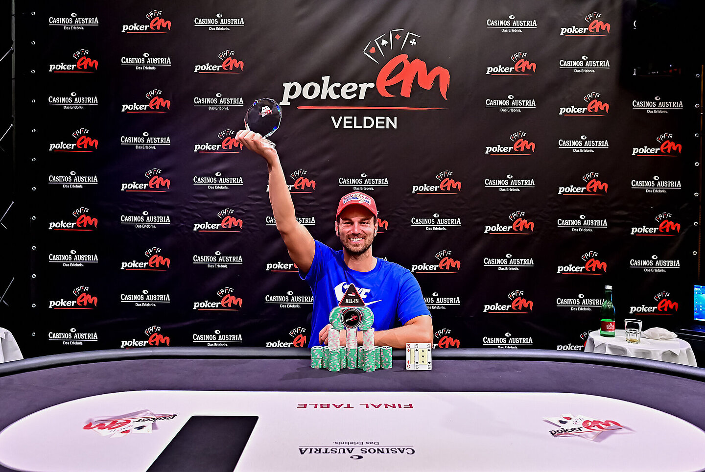 Gewinner sitzt am Pokertisch und hält seinen Pokal hoch