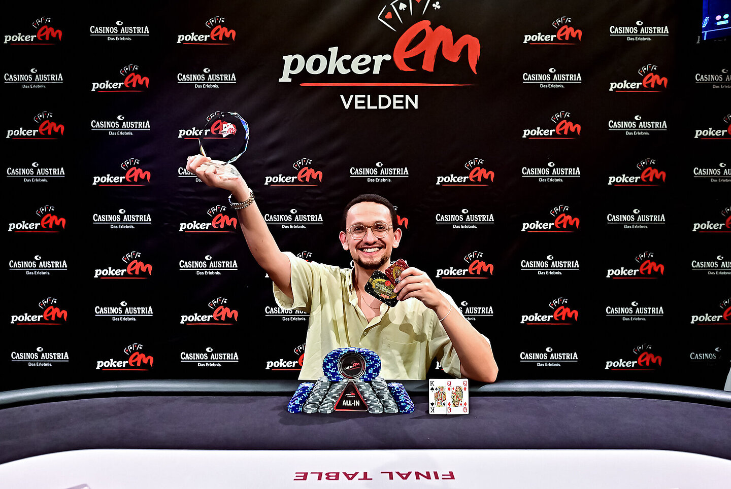 Der Gewinner sitzt am Final Table und hält seinen Pokal hoch. 