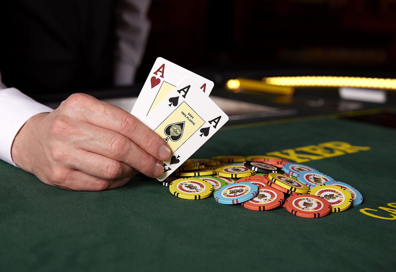 Herrenhand in weißem Hemd am Pokertisch lehnend hält zwei Asse, nebenbei Jetons