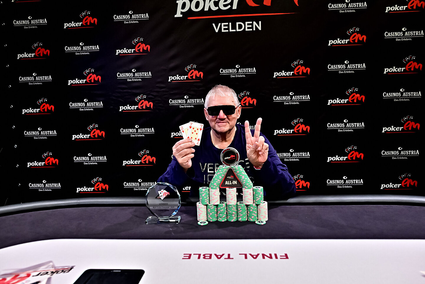 Der Gewinner sitzt am Final Table und hält zwei Spielkarten in der Hand.