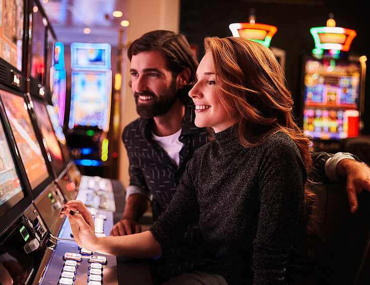 Casinos Austria Frau und Mann spielen an den Spielautomaten im Casino
