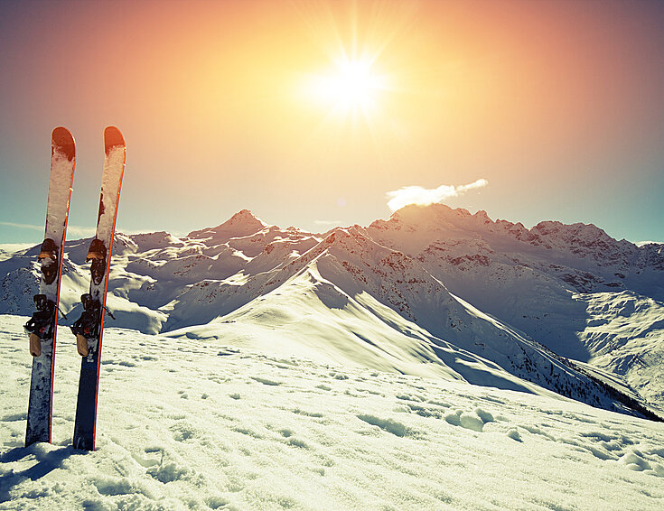 Ein Paar Ski vor einem Bergpanorama bei Sonnenuntergang