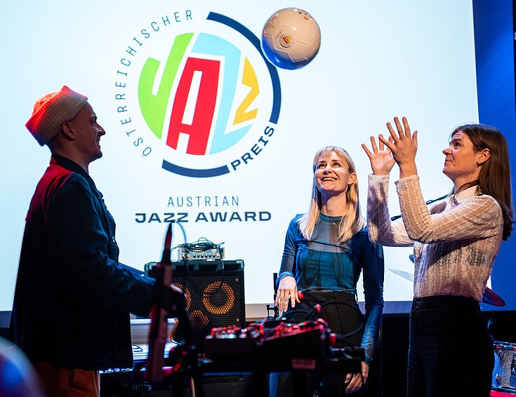 (c) Österreichischer Musikrat Drei Menschen stehen auf einer Bühne vor Musikinstrumenten