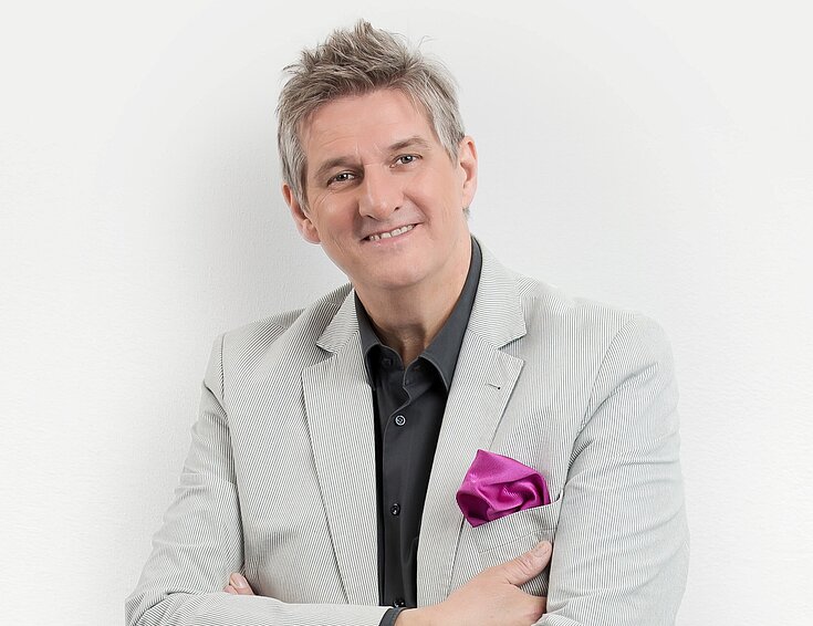 (c) Silvio Samoni Ein älterer Herr steht festlich gekleidet vor einer Wand