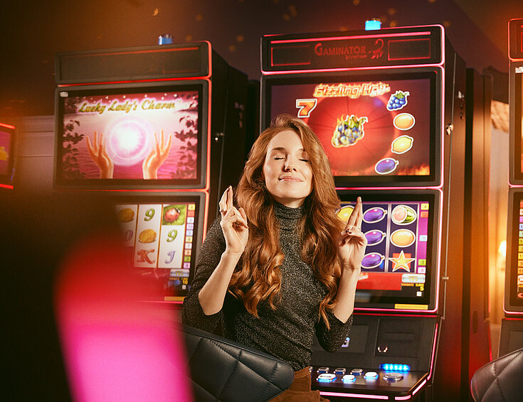 Casinos Austria Dame mit gekreuzten Fingern vor den Spielautomaten