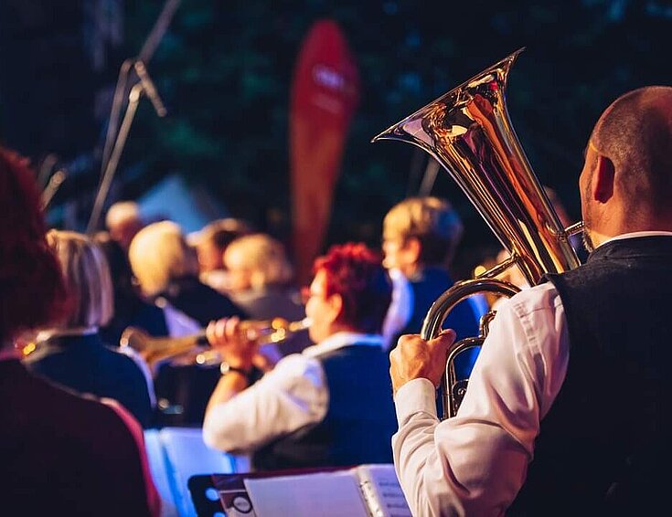 Musiker mit unterschiedlichen Instrumenten sitzen vor Notenbüchern