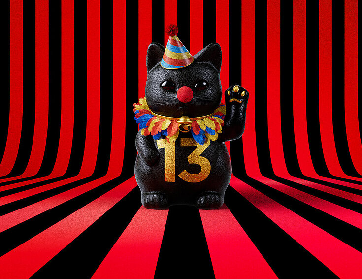 13er Glückskatze mit Faschings-Hut auf rot-schwarz-gestreiftem Hintergrund