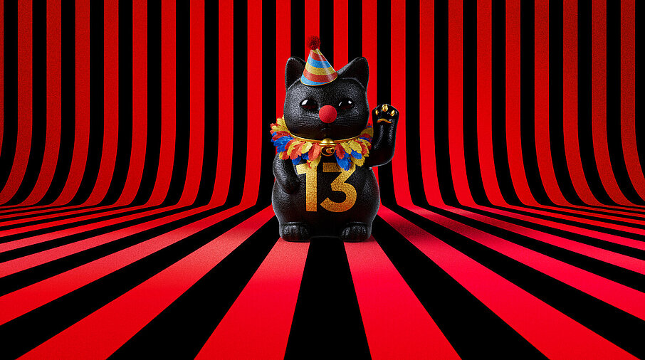 13er Glückskatze mit Faschings-Hut auf rot-schwarz-gestreiftem Hintergrund