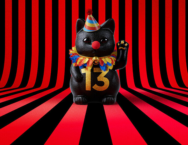 13er Glückskatze mit Faschings-Hut auf rot-schwarz-gestreiftem Hintergrund