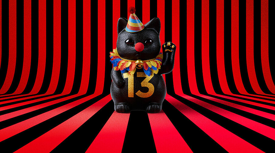 13er Glückskatze mit Faschings-Hut auf rot-schwarz-gestreiftem Hintergrund
