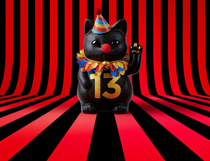 13er Glückskatze mit Faschings-Hut auf rot-schwarz-gestreiftem Hintergrund