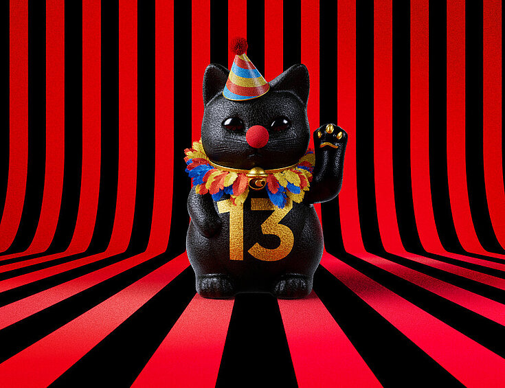 13er Glückskatze mit Faschings-Hut auf rot-schwarz-gestreiftem Hintergrund