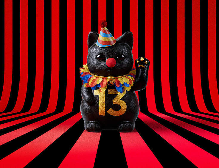 13er Glückskatze mit Faschings-Hut auf rot-schwarz-gestreiftem Hintergrund