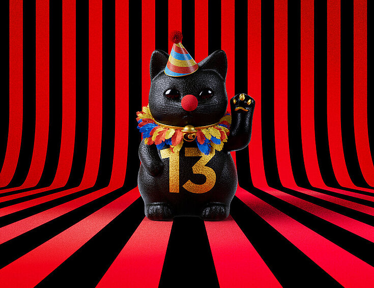 13er Glückskatze mit Faschings-Hut auf rot-schwarz-gestreiftem Hintergrund