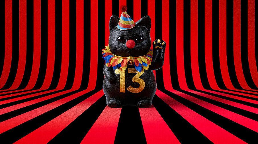13er Glückskatze mit Faschings-Hut auf rot-schwarz-gestreiftem Hintergrund