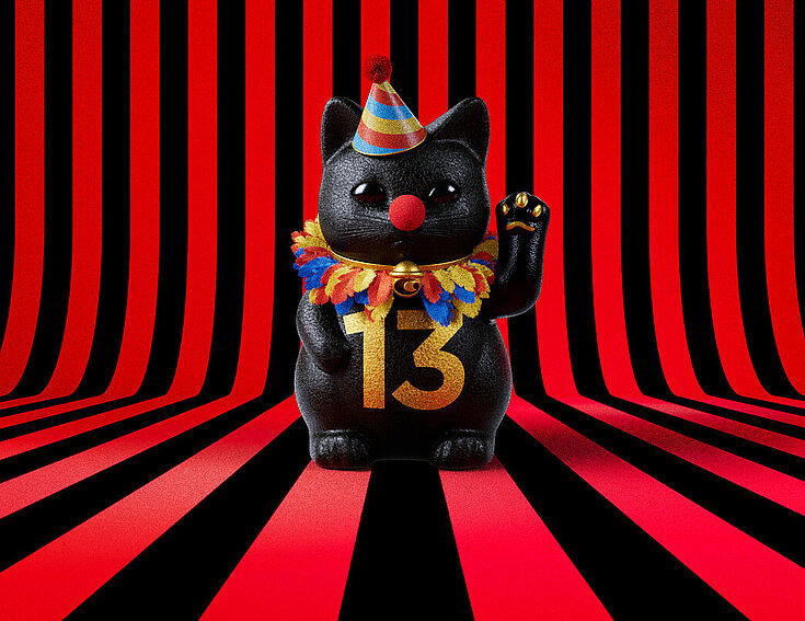 13er Glückskatze mit Faschings-Hut auf rot-schwarz-gestreiftem Hintergrund