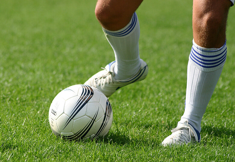 Fußballer-Beine und Fußball auf grünem Rasen