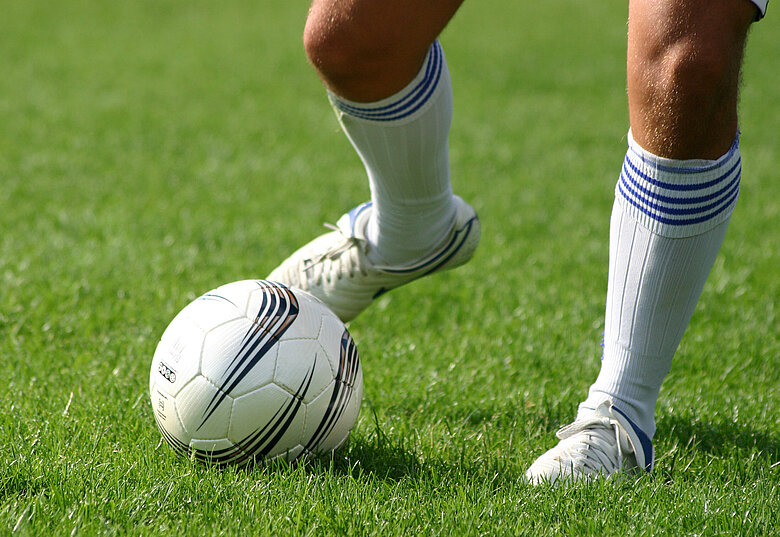 Fußballer-Beine und Fußball auf grünem Rasen