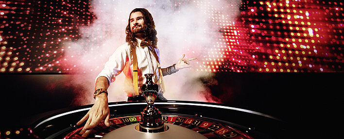 Game Zone Croupier mit Rauch und MEGA LED Wall im Hintergrund und Roulettekessel
