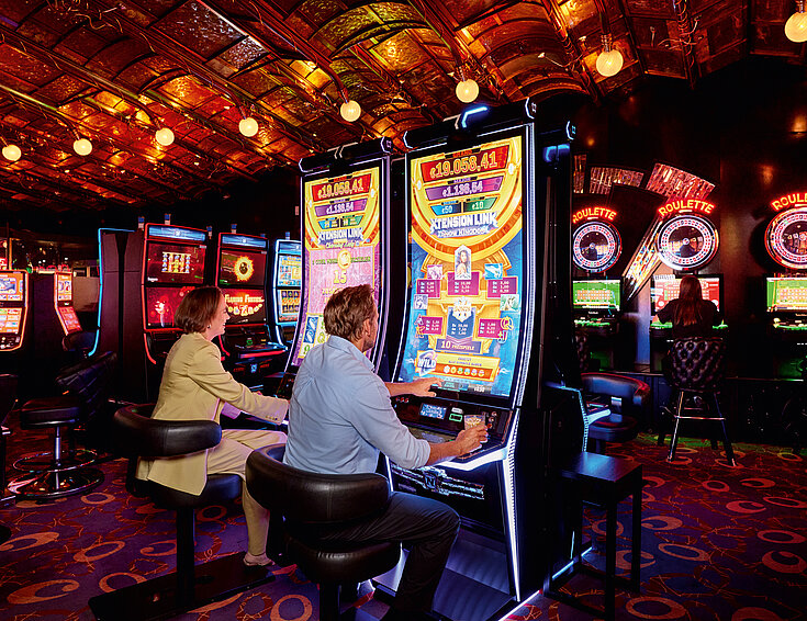 Mann und Frau sitzen vor den Automaten und spielen 