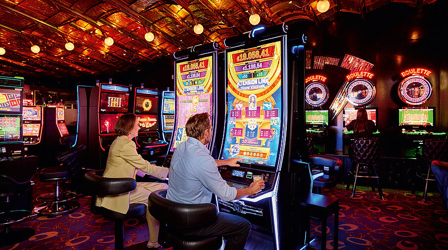 Mann und Frau sitzen vor den Automaten und spielen 