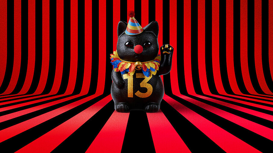 13er Glückskatze mit Faschings-Hut auf rot-schwarz-gestreiftem Hintergrund