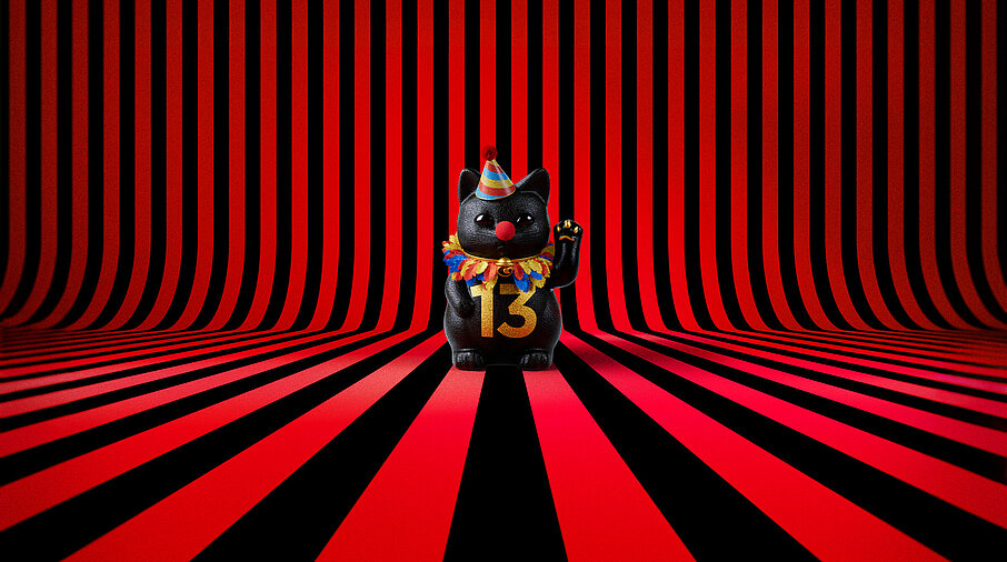 13er Glückskatze mit Faschings-Hut auf rot-schwarz-gestreiftem Hintergrund