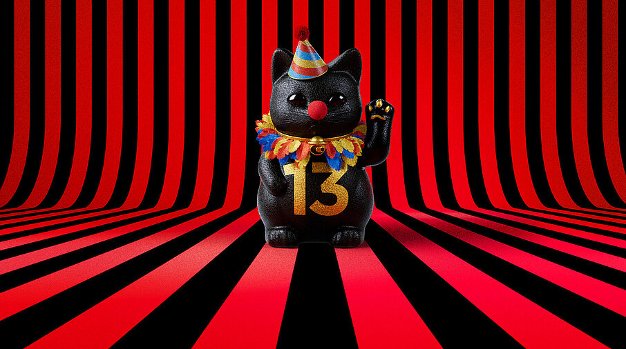 13er Glückskatze mit Faschings-Hut auf rot-schwarz-gestreiftem Hintergrund