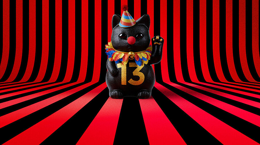 13er Glückskatze mit Faschings-Hut auf rot-schwarz-gestreiftem Hintergrund