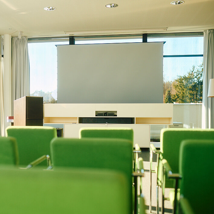 Heller Seminarraum mit Leinwand mit Tischen und Stühlen