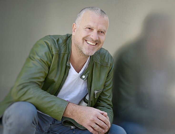 (c) www.fotowerk.at Bernhard Aichner sitzt da und lacht.