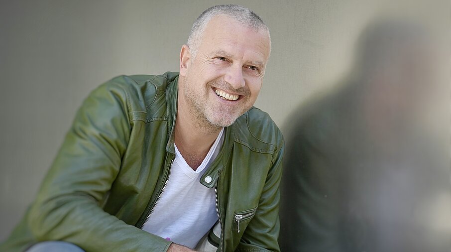 Bernhard Aichner sitzt da und lacht. 